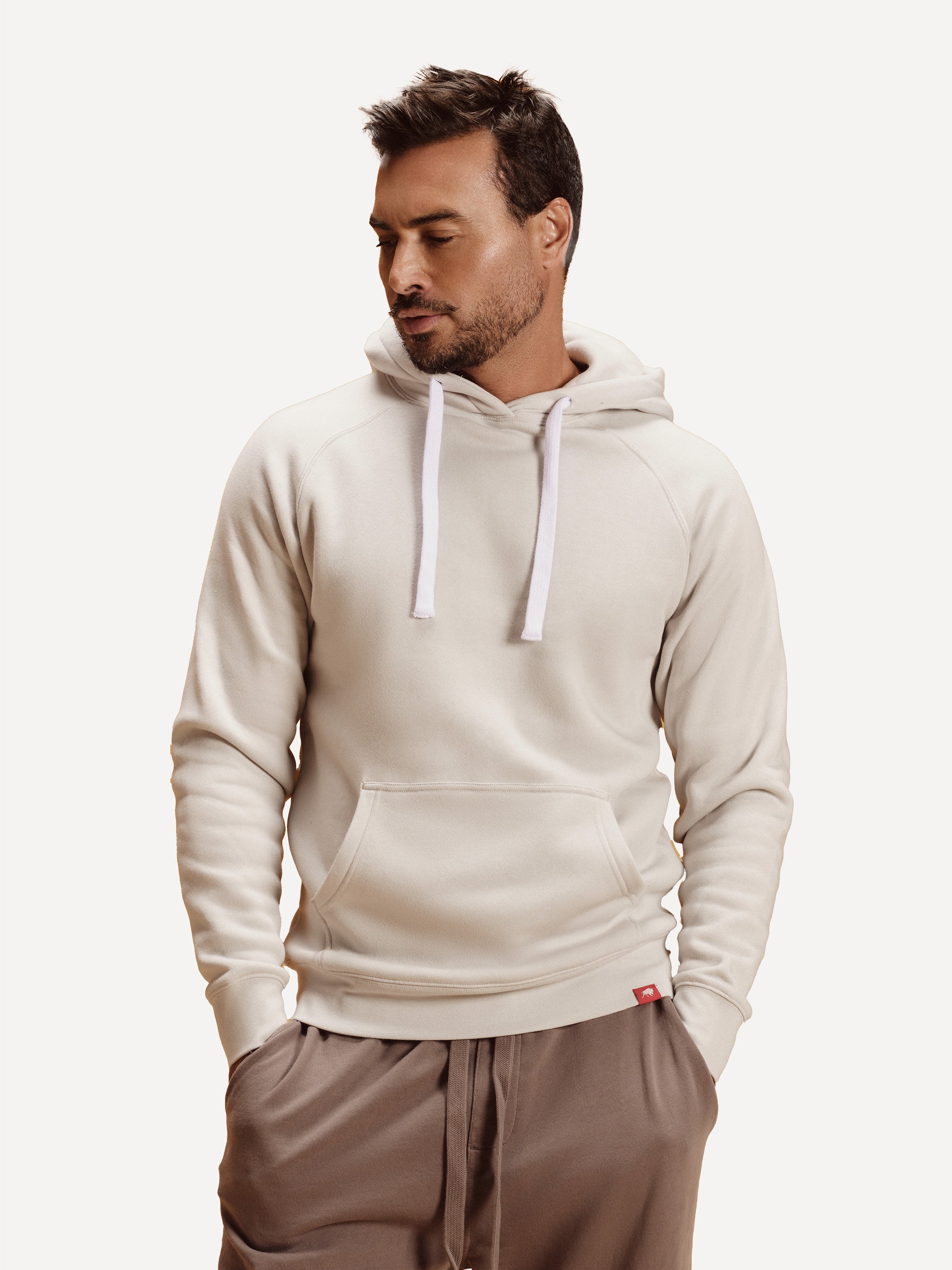 Man wearing a beige hoodie with white drawstrings on a plain background
